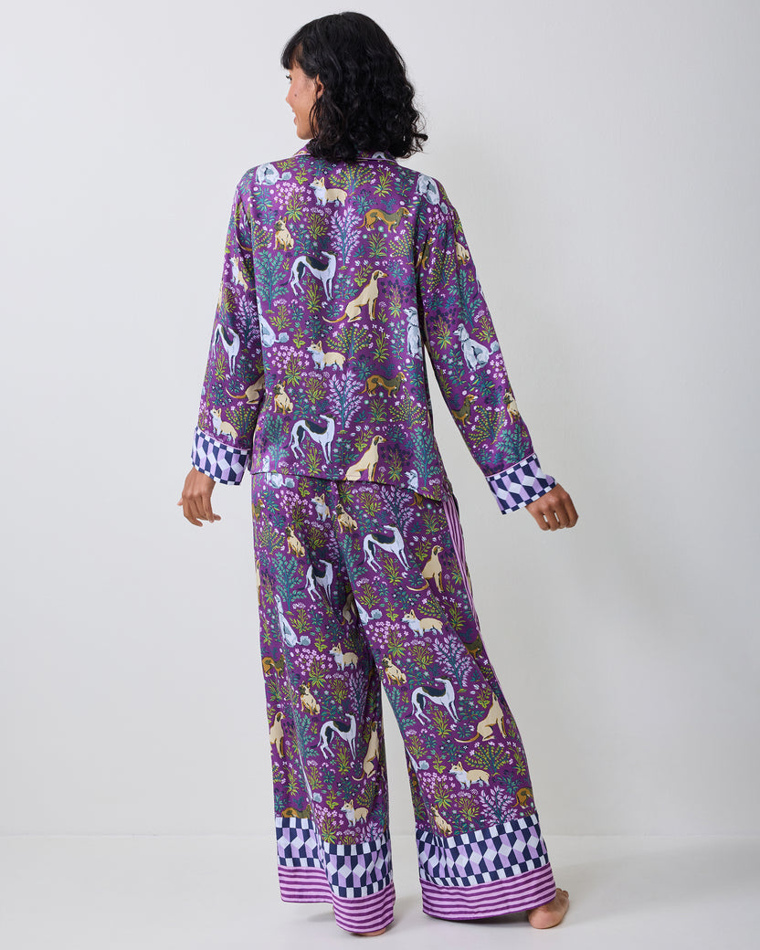 Back view of a purple dog-and-floral print pajama set with a long-sleeve button-front top and wide-leg pants, both finished with geometric cuffs and hems.