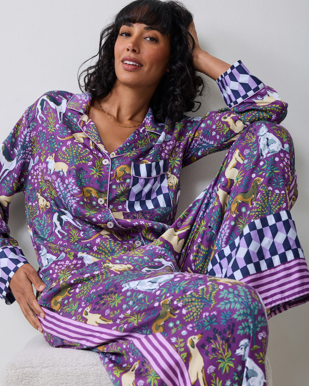 Person seated wearing a purple dog-and-floral print pajama set with a button-front top, chest pocket, wide-leg pants, and geometric cuffs and hems.