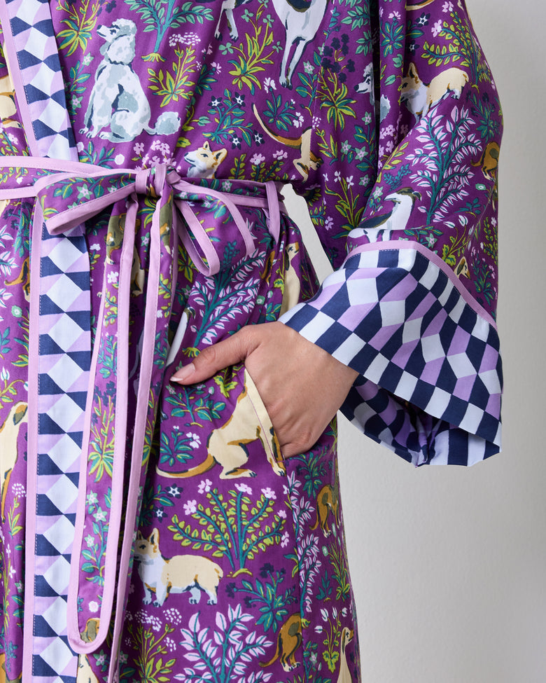 Close-up of a purple dog-and-floral print wrap robe showing the tied belt, side pocket, contrasting trim, and wide sleeve cuff.
