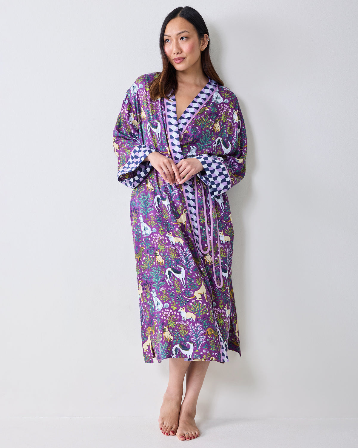 Front three-quarter view of a person wearing a purple dog-and-floral print wrap robe with contrasting trim, wide cuffs, and a belt tied at the waist.