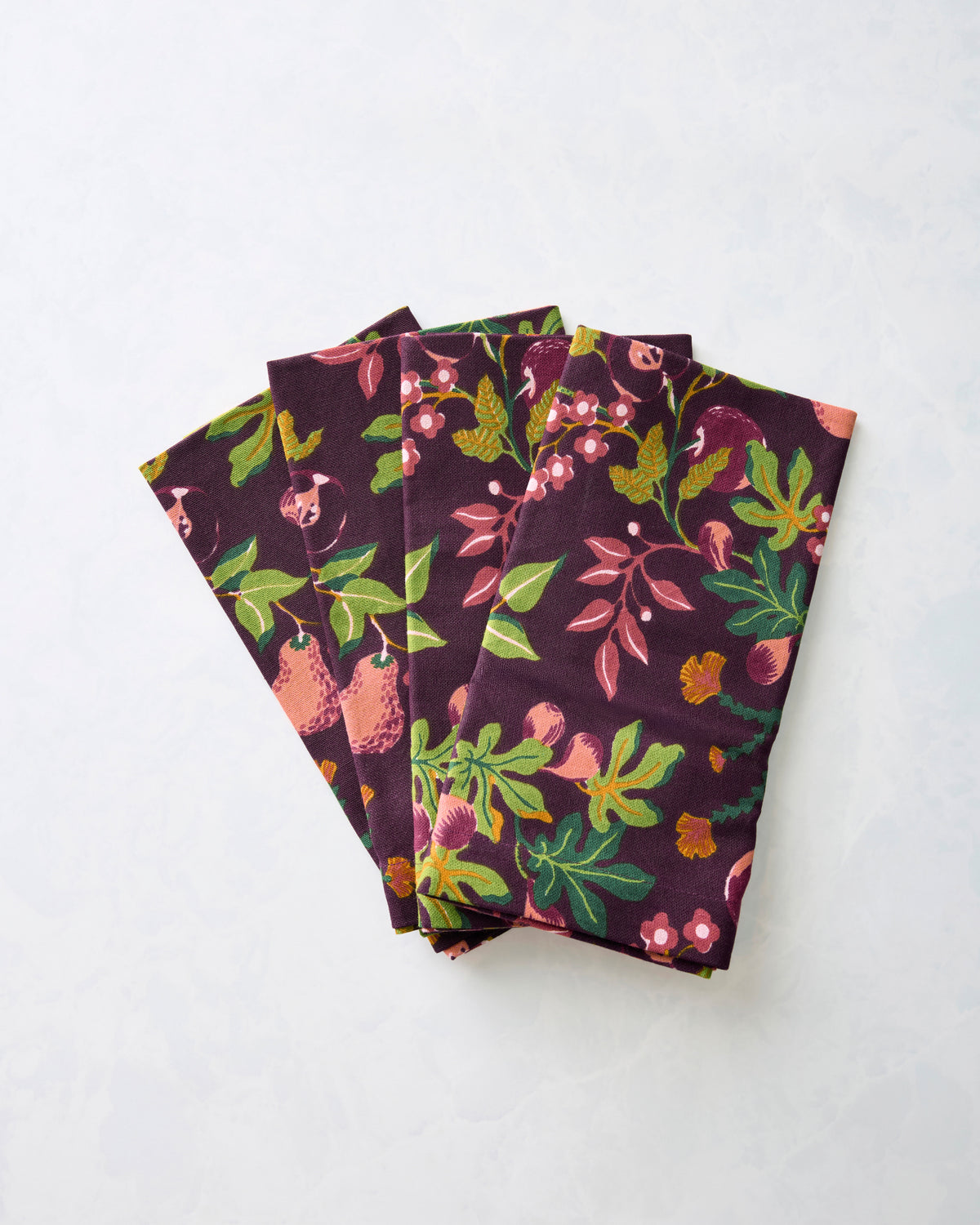 Four folded Pomme & Poire dinner napkins in a plum fruit-and-floral print.