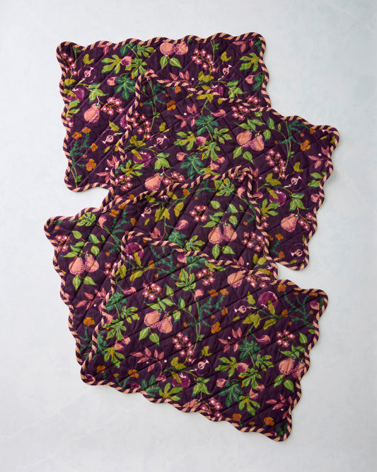Four overlapping quilted Pomme & Poire placemats with scalloped edges and a plum fruit-and-floral print.