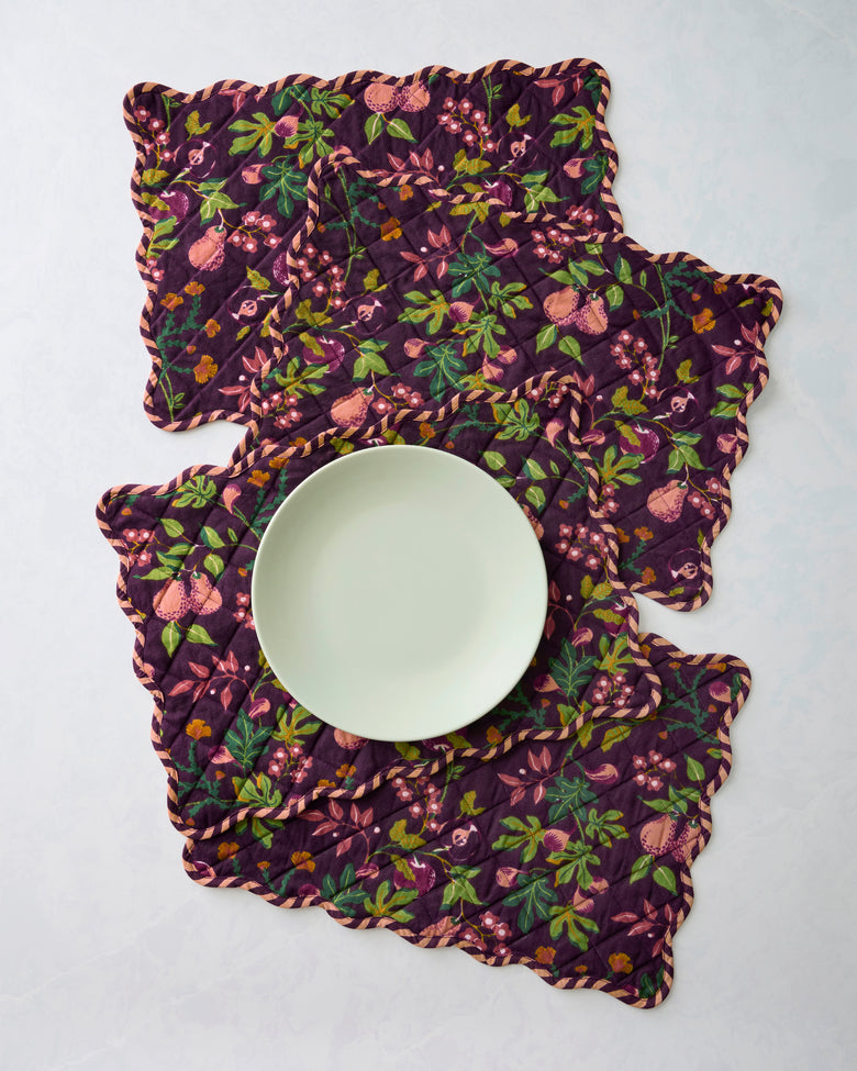 Four overlapping quilted Pomme & Poire placemats with scalloped edges; a plate is centered on the front placemat.