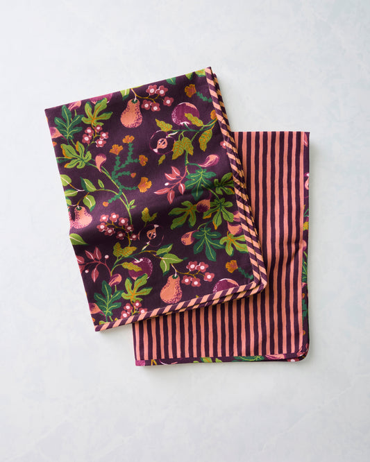 Two Pomme & Poire plum tea towels folded and overlapping, showing the fruit and floral print on one side and stripes on the other.