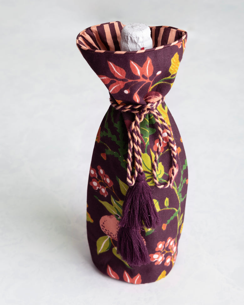 Plum floral wine bag holding a bottle, with a braided tie and tassels at the neck.