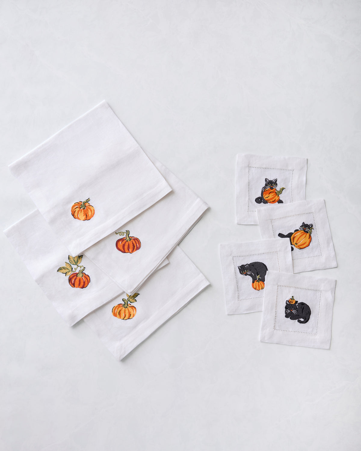 White napkin bundle with embroidered pumpkins on four dinner napkins and four cocktail napkins.