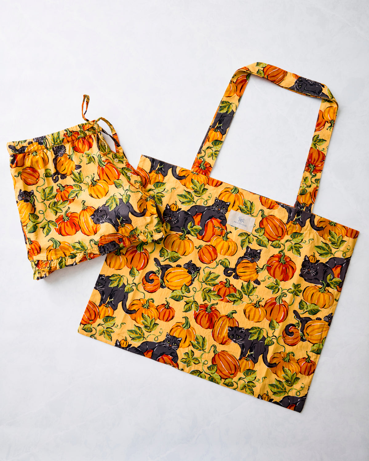 Pumpkin and black-cat print ruffle shorts beside a matching tote bag.