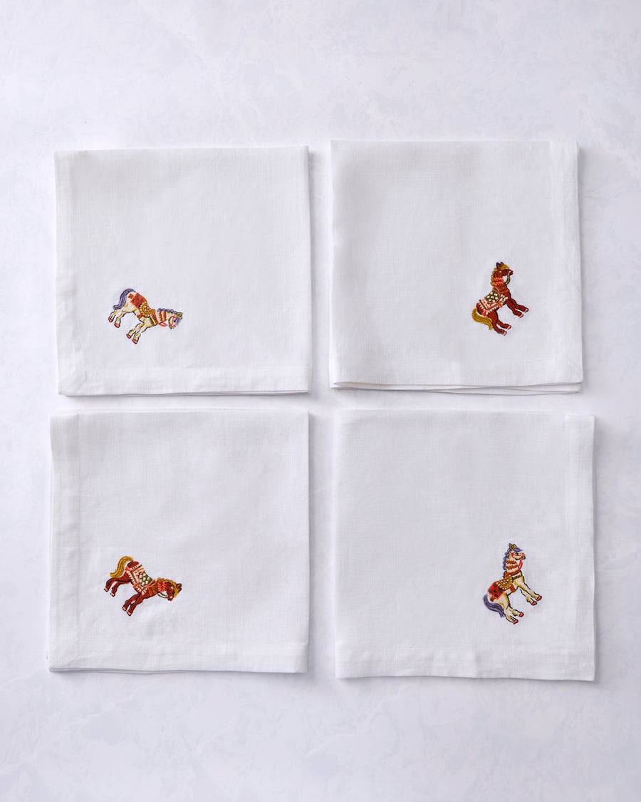 Four white dinner napkins arranged in a square, each with an embroidered horse in a different pose.