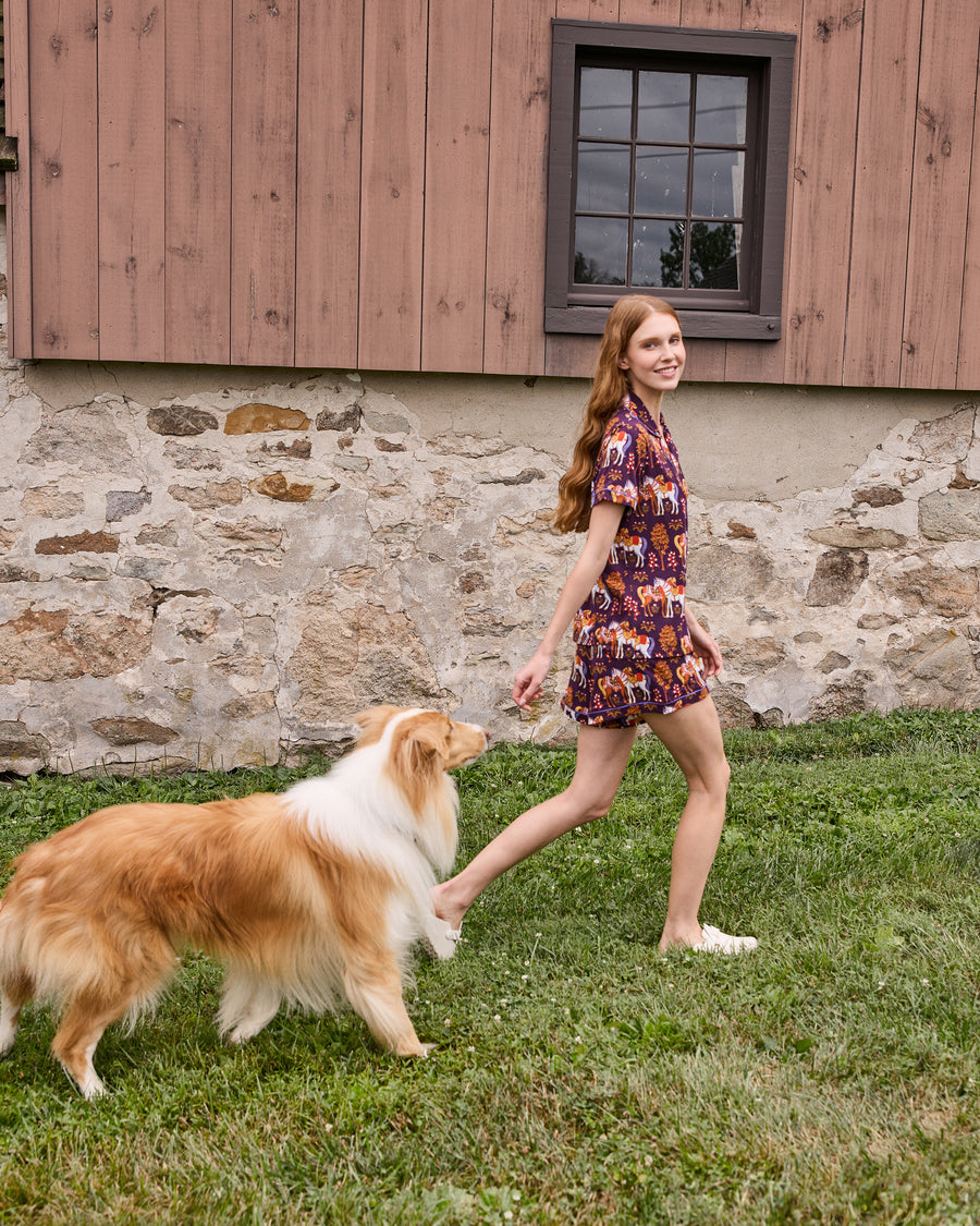 Person wearing the short-sleeve Queen’s Horses pajama set walking with a collie outdoors.