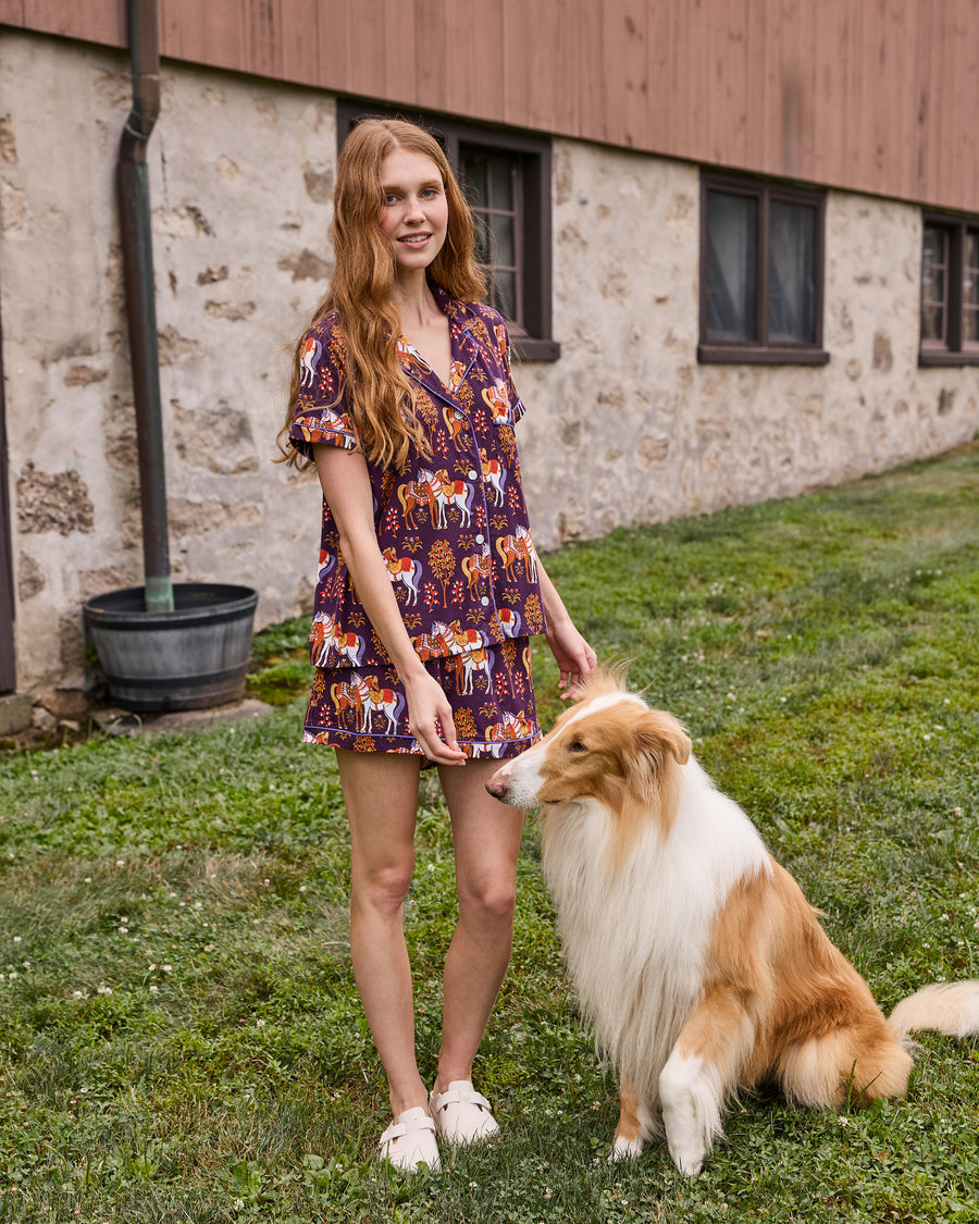 Person wearing the short-sleeve Queen’s Horses pajama set standing beside a seated collie outdoors.