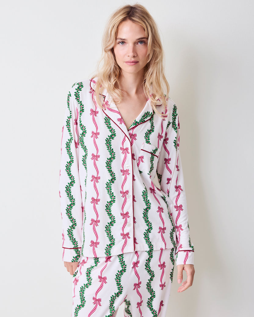Front view of a person wearing the Ribbons & Bows button-down pajama set with pink bow and green garland print.