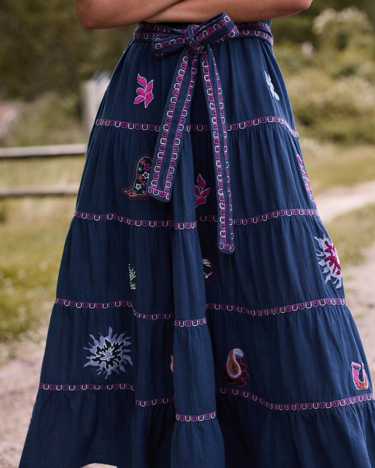 Close-up of the navy To and From dress showing the tied waist belt, tiered skirt, embroidered motifs, and decorative trim.