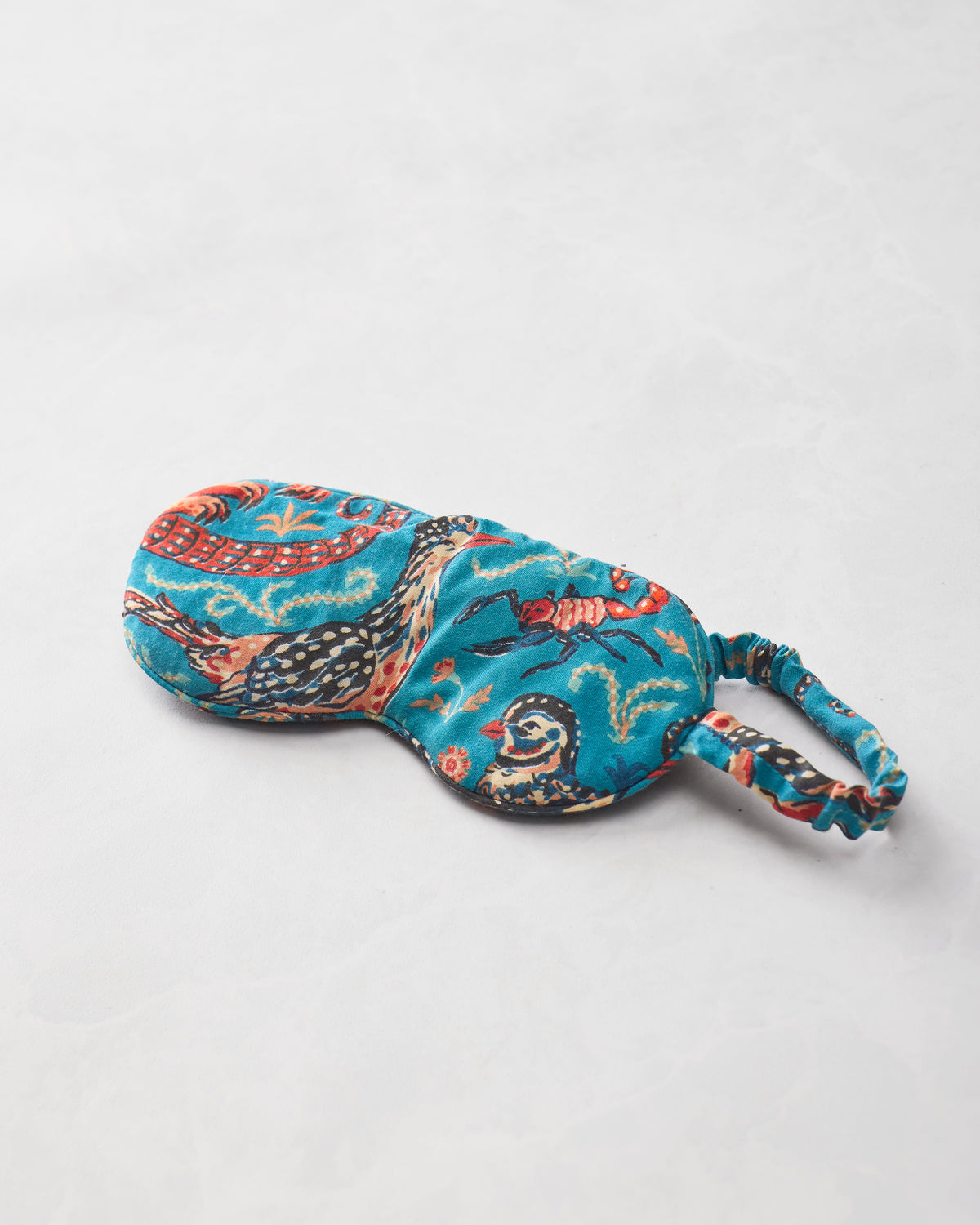 Close-up of the teal Canyon Critters eye mask on a light background, showing lizards, a bird, an armadillo, and an insect in the print.