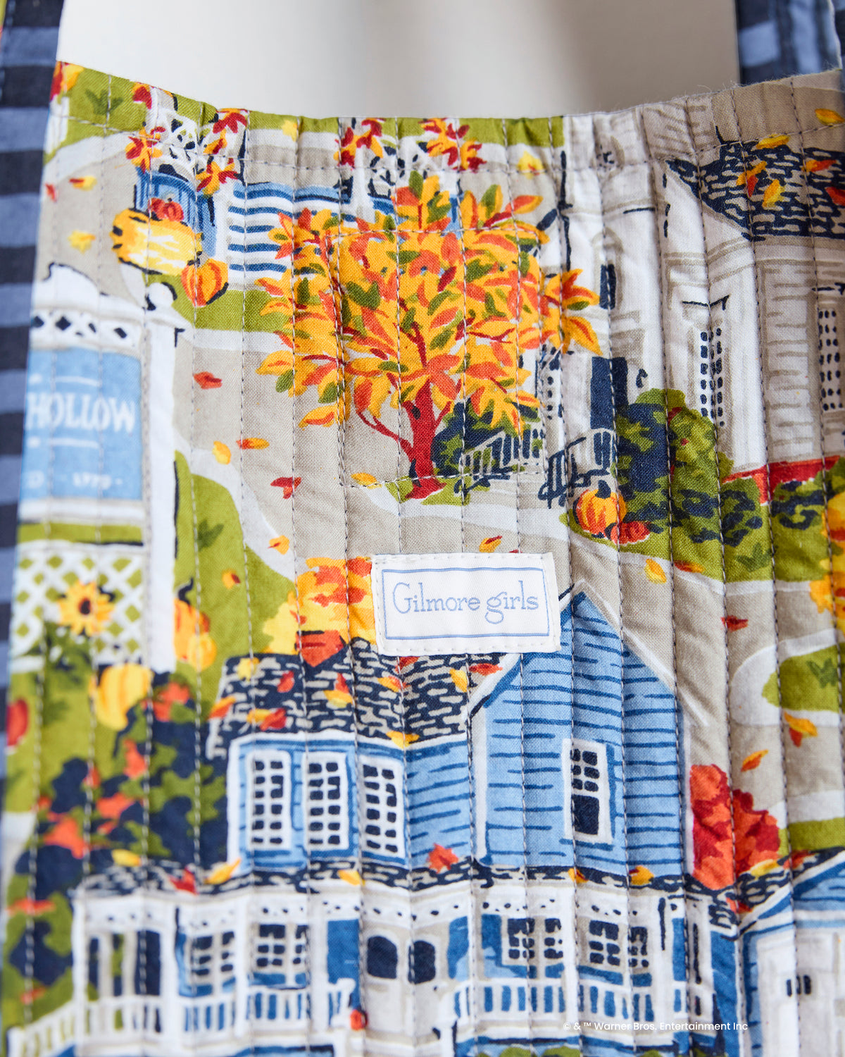 Close-up of the Stars Hollow Traveler Tote print showing autumn trees, illustrated buildings, and a sewn Gilmore Girls label.