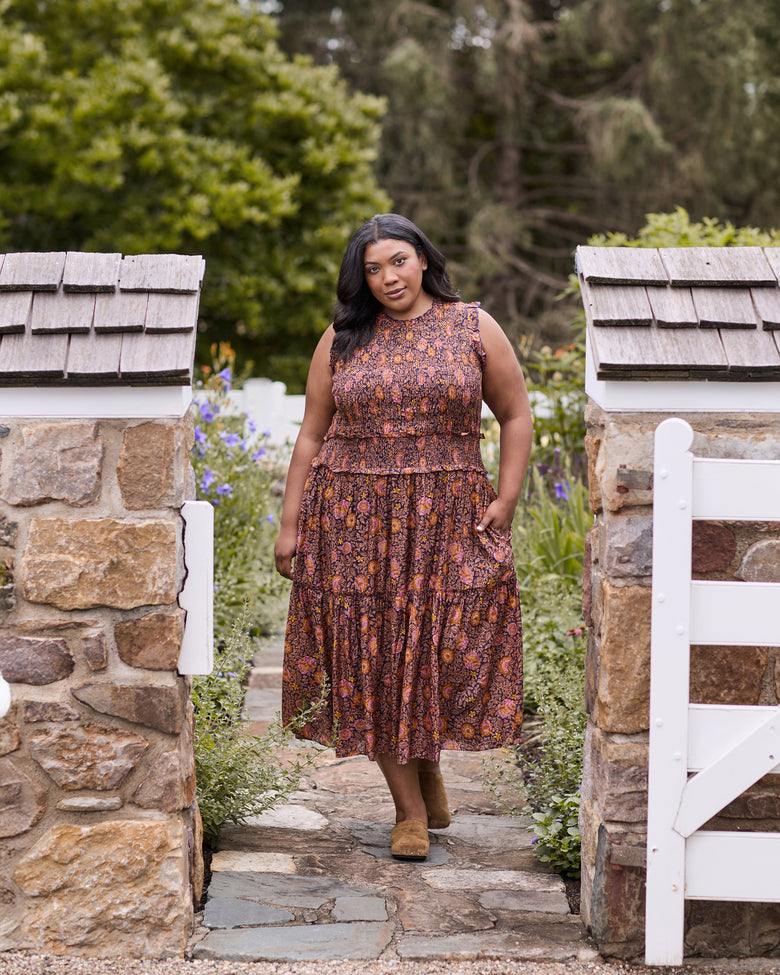 Full-length view of the Sunset Vine Ellis dress, showing the sleeveless bodice, smocked waist, tiered skirt, floral print, and side pockets.