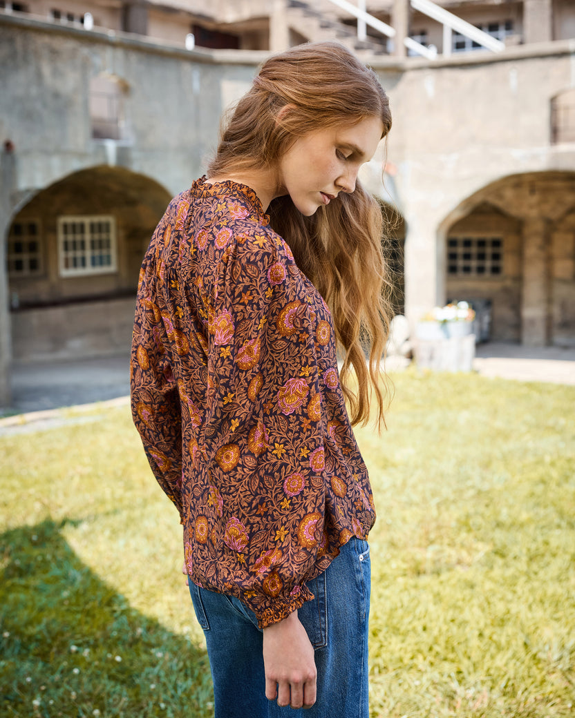 Back and side view of the Sunset Vine Evelyn blouse, showing its long sleeves, gathered cuffs, curved hem, and floral print.