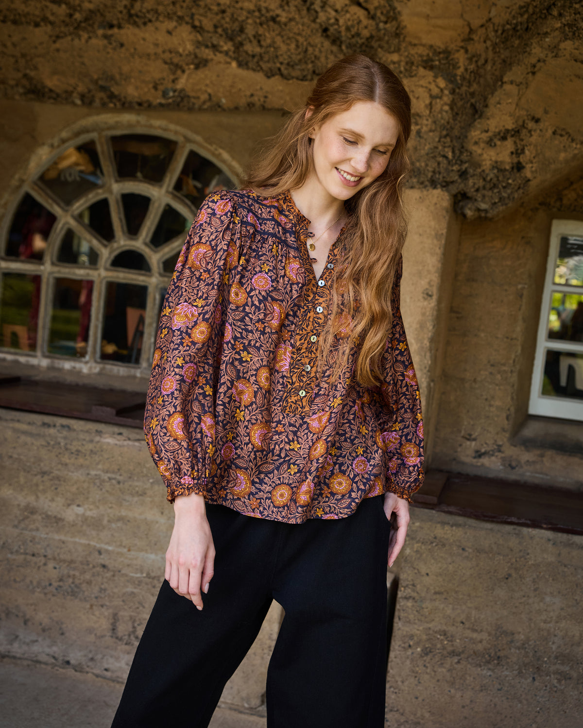 Front three-quarter view of the Sunset Vine Evelyn blouse, showing its V-neckline, button placket, long sleeves, gathered cuffs, and floral print.