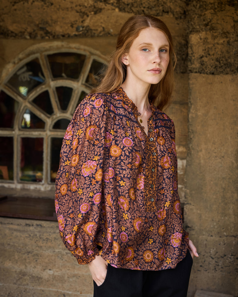 Front view of the Sunset Vine Evelyn blouse, showing its V-neckline, button placket, long sleeves, gathered cuffs, curved hem, and floral print.