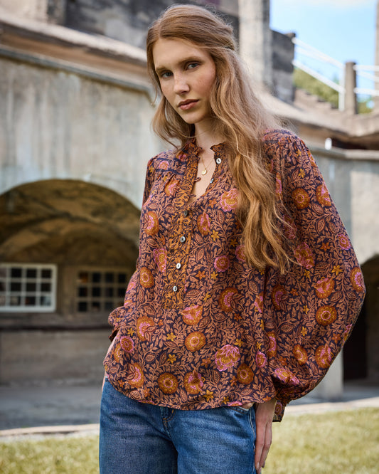 Model wearing the Sunset Vine Evelyn Blouse with a floral patterned print, button-front neckline, long sleeves, and jeans.