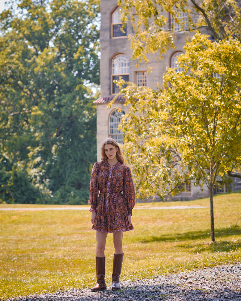 Full-length view of the Sunset Vine Soleil Dress with long sleeves, button front, tie waist, and tiered skirt in a park setting.