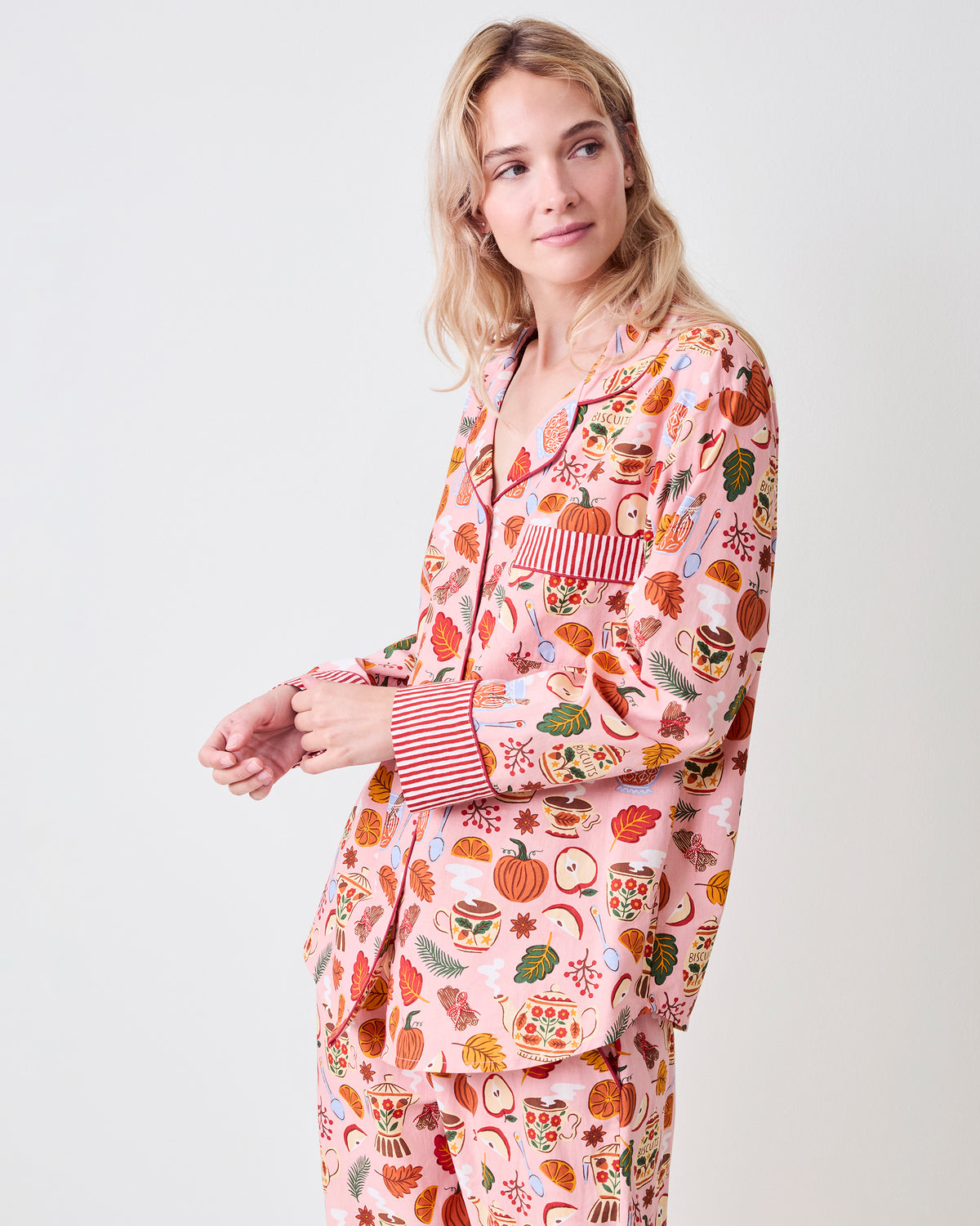 Three-quarter view of the pink Autumn Cafe petite long pajama set, showing the button-front top, chest pocket, striped cuffs, matching pants, and tea and autumn print.