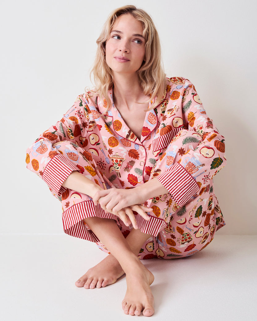 Person seated on the floor wearing the pink Autumn Cafe tall long pajama set, showing the notched collar, striped cuffs, matching pants, and tea and autumn print.