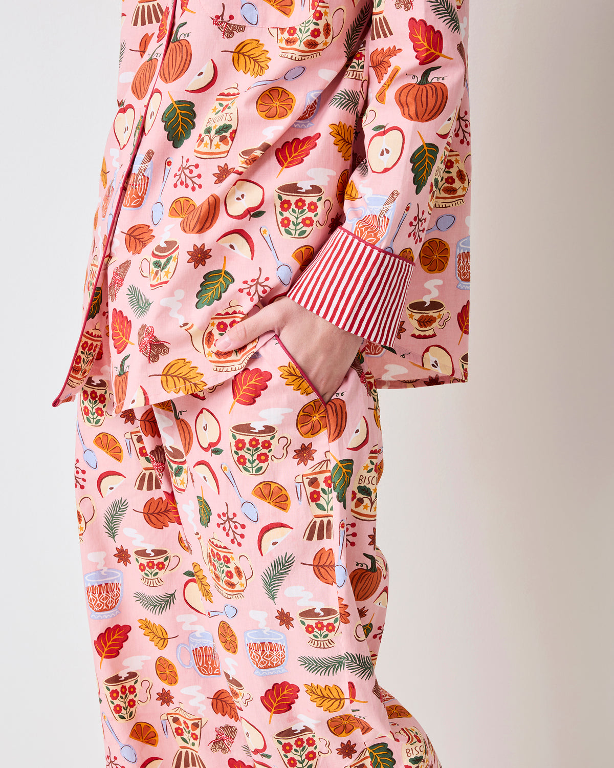Close-up of the pink Autumn Cafe pajama top and matching pants, showing a striped cuff, side pocket, buttons, and tea, fruit, leaf, and biscuit-jar print.