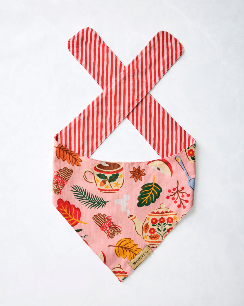 Pet bandana displayed flat with a pink tea-and-autumn print, red-and-white striped tie straps, and a pointed lower edge.