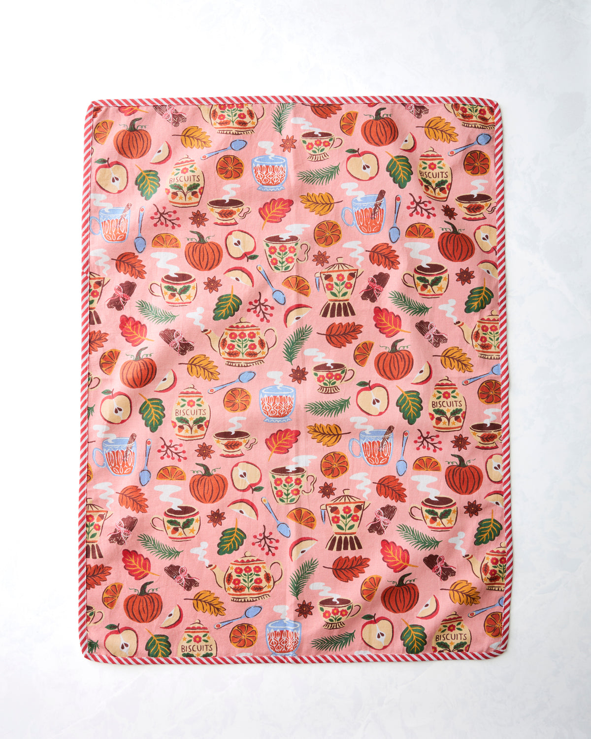 Front of a tea towel with a rose pink repeating print of teapots, cups, pumpkins, fruit, leaves, and spoons.