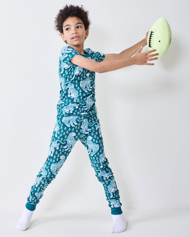 Child wearing a teal tiger-print short-sleeve pajama set reaches toward a football.