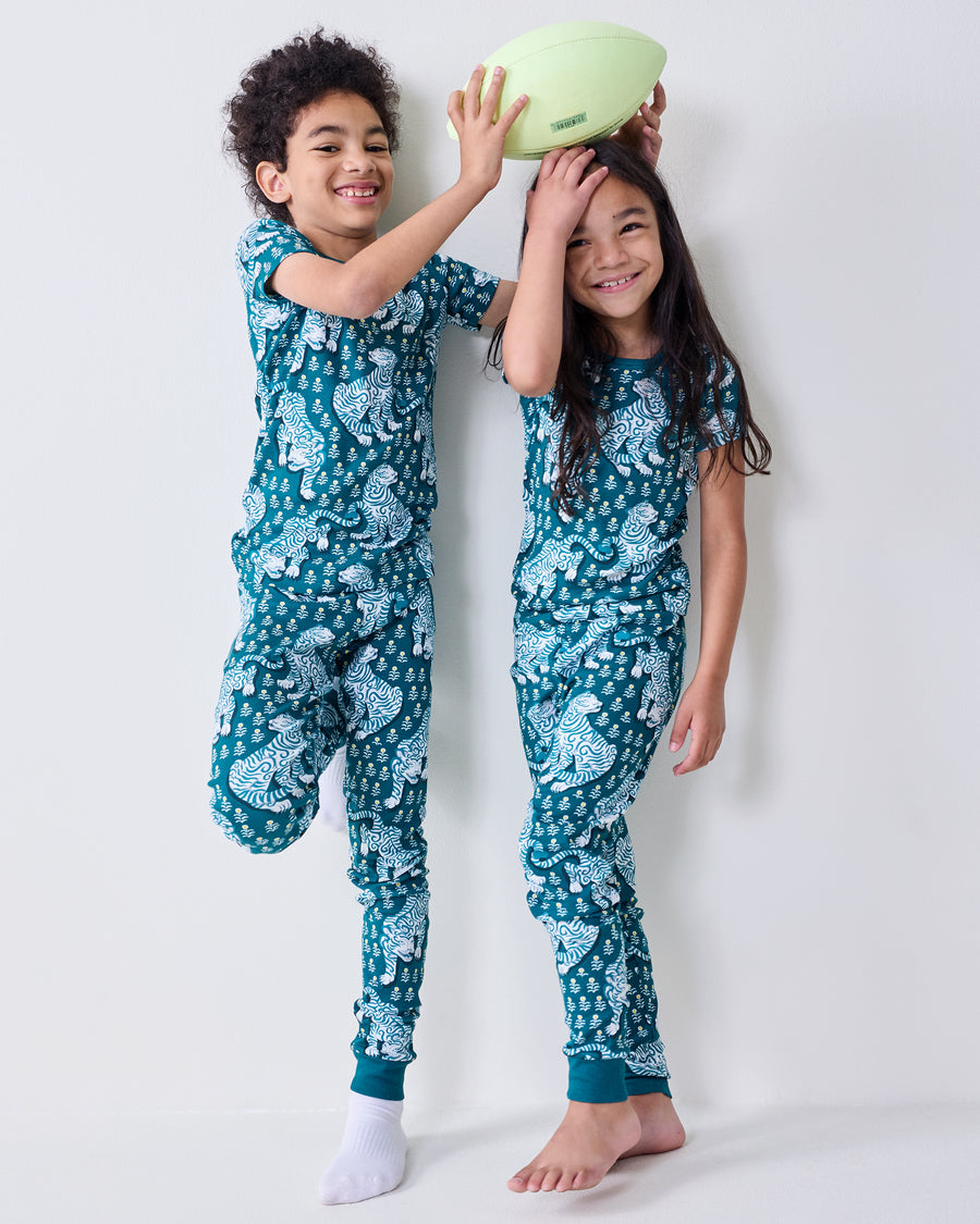 Two children wear matching tiger-print short-sleeve pajama sets; one holds a football above the other's head.