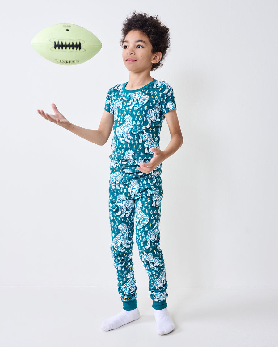 Child wearing a teal tiger-print short-sleeve pajama set reaches toward a floating football.