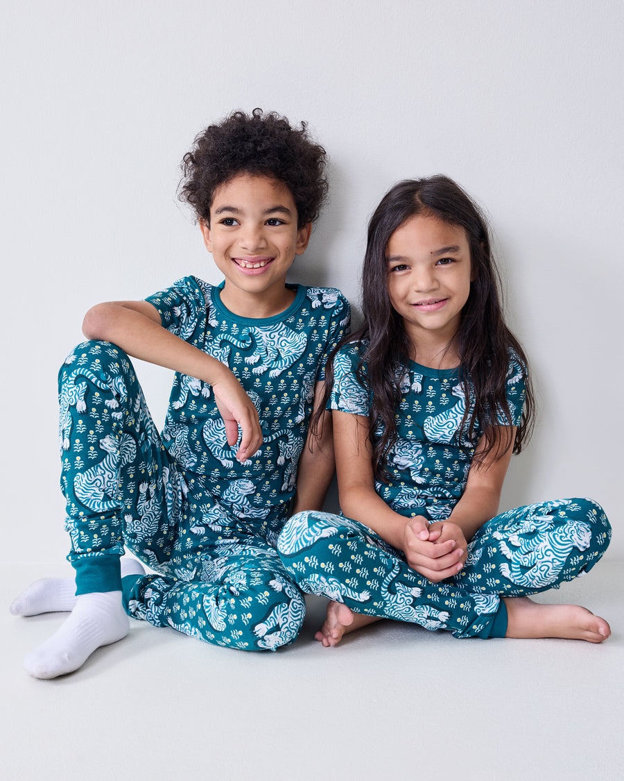 Two children wearing matching teal pajama sets with white tiger and wave patterns.