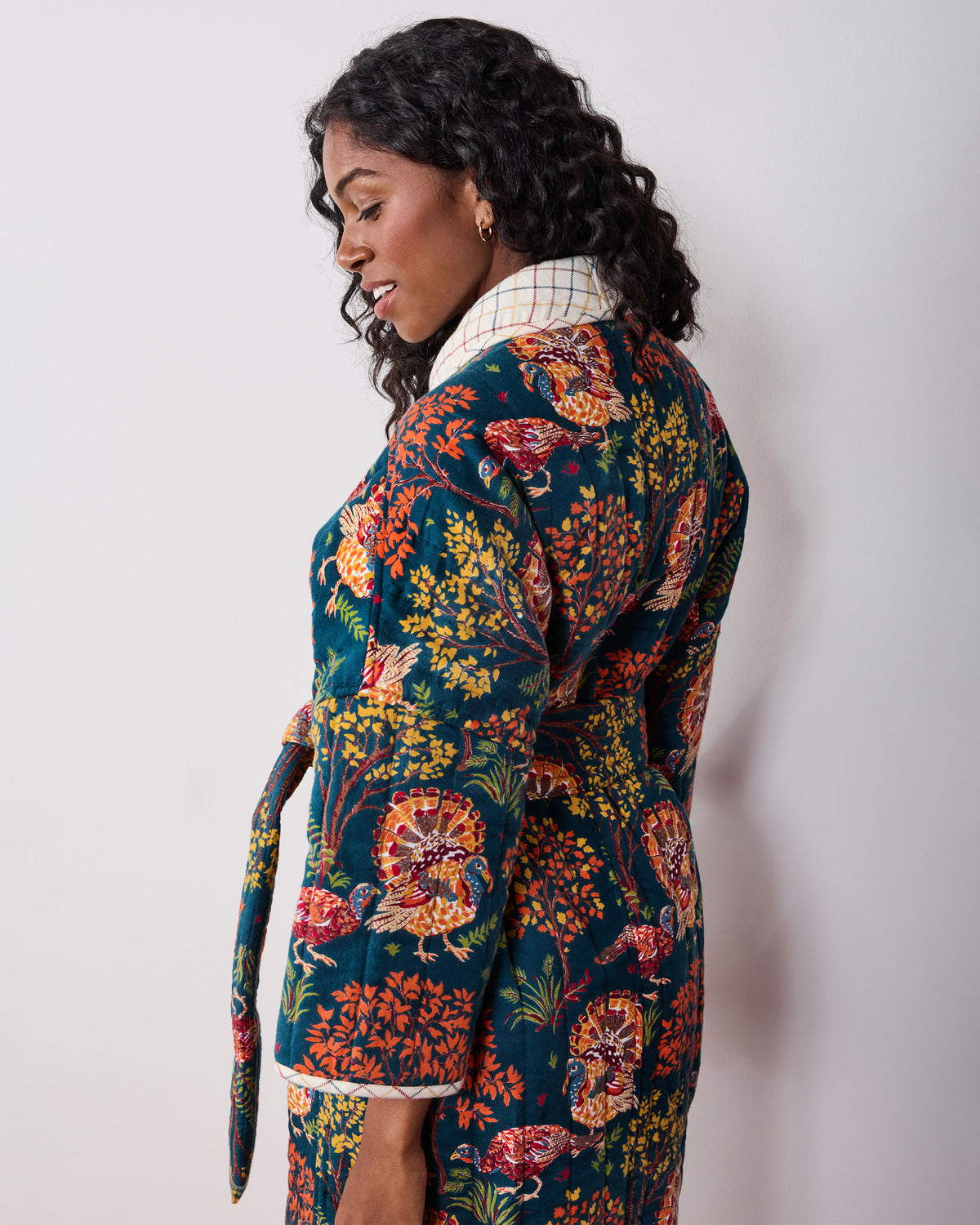 Back three-quarter view of a navy Turkey Trot robe with colorful turkey-and-floral print, plaid collar and cuffs, and waist tie.