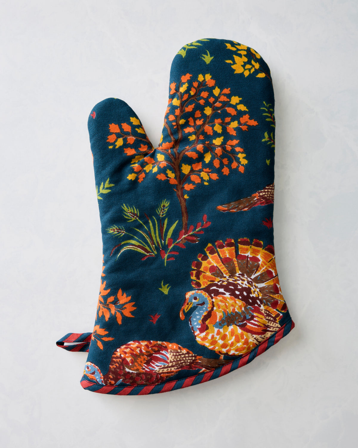Navy oven mitt with a colorful turkey and autumn foliage print, shown from the opposite hand orientation.