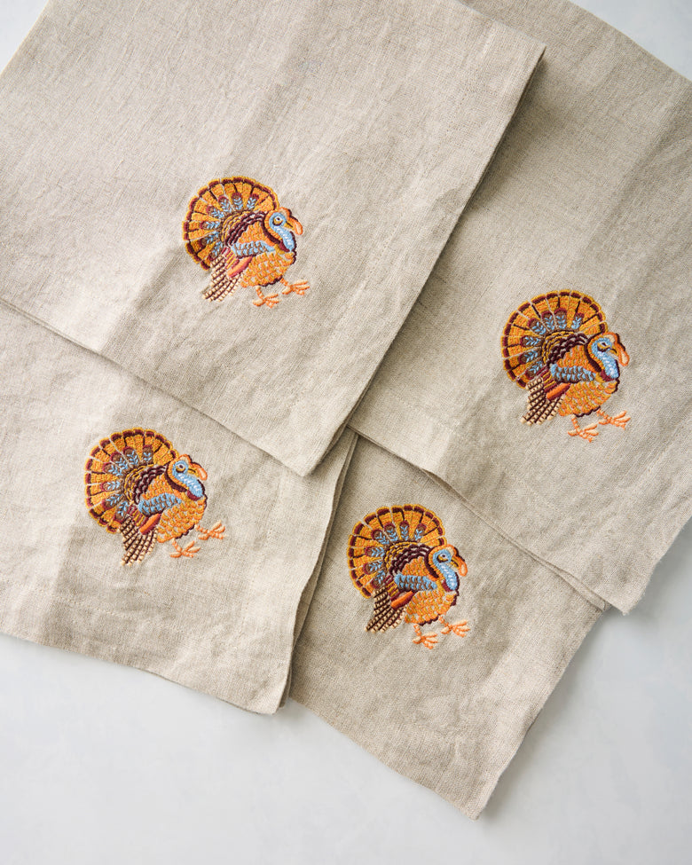 Close-up of four natural napkins with matching embroidered turkey motifs.