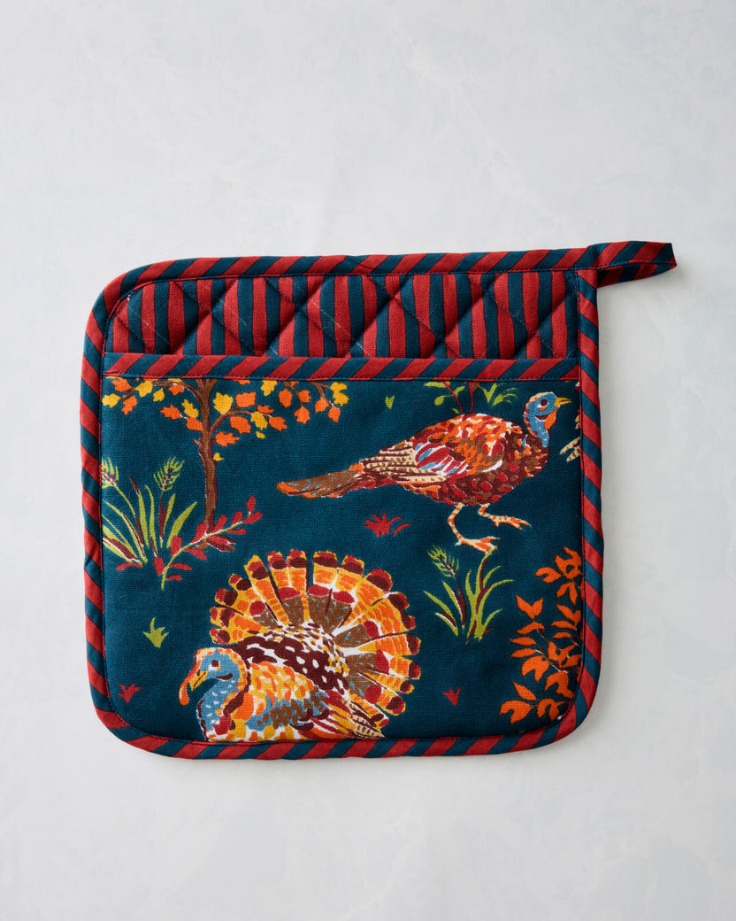 Navy pot holder with a colorful turkey and foliage print, red-and-navy striped edging, and a hanging loop.