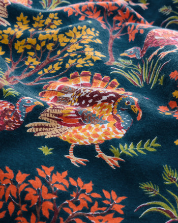 Close-up of a dark teal pattern with illustrated turkeys, autumn trees, grasses, and colorful foliage.