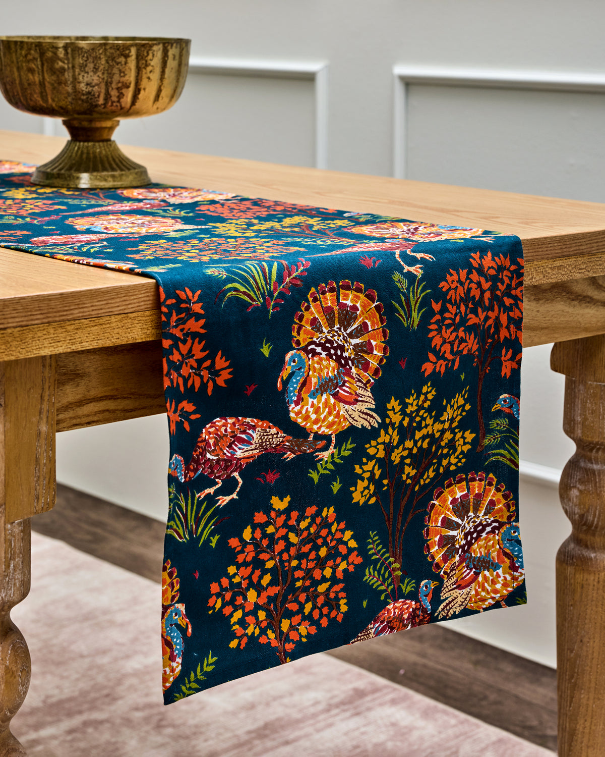 Navy Turkey Trot table runner with printed turkeys, trees, and foliage draped over a wooden table.