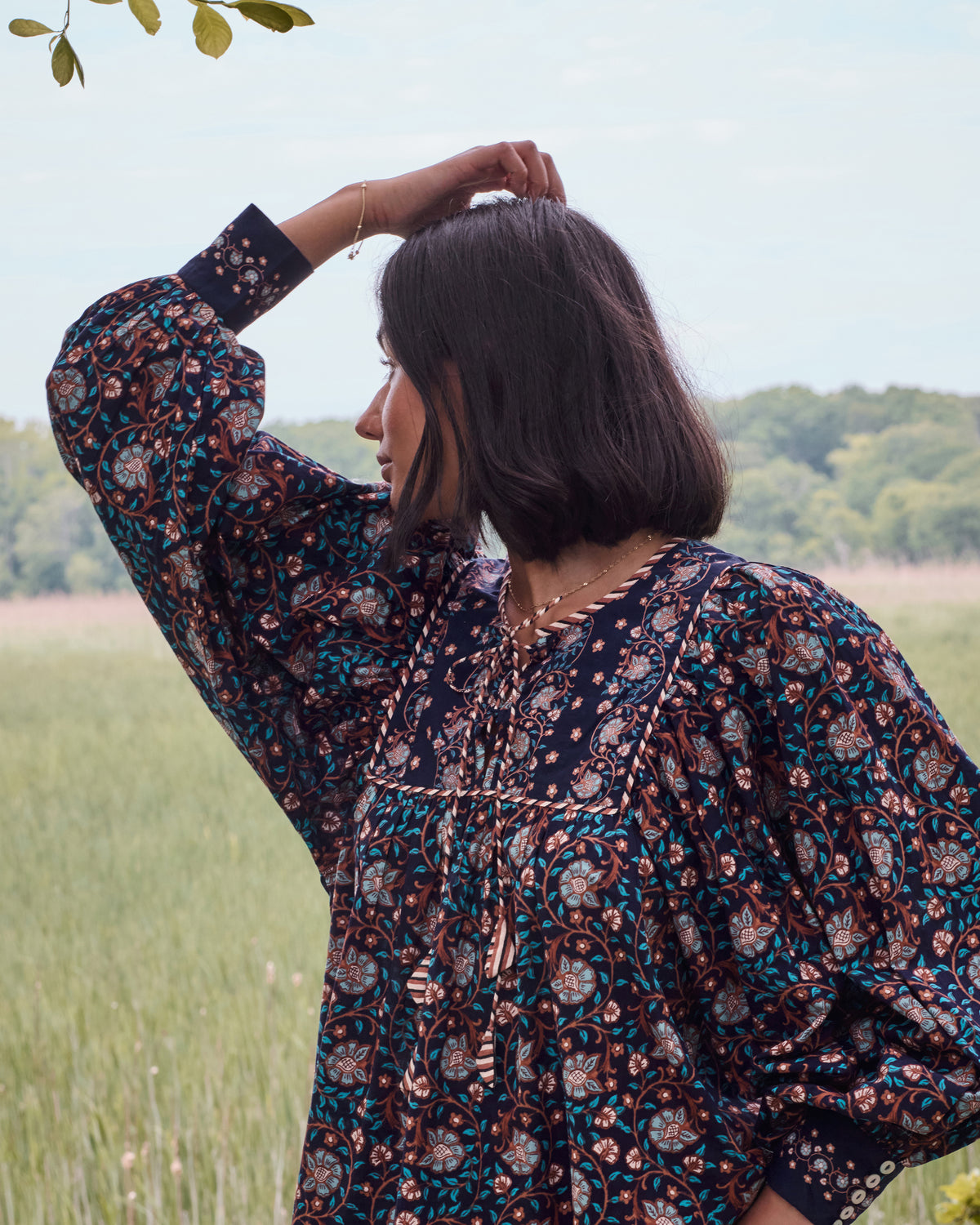 Side view of the Valley Garden Josephine blouse showing the floral print, criss-cross neckline, tassel ties, and full sleeve.