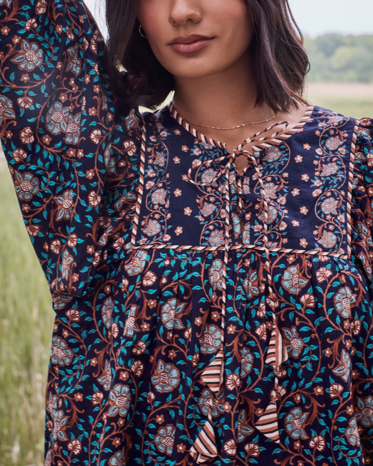 Close view of the Valley Garden Josephine blouse in a dark floral print, showing the criss-cross neckline, tassel ties, and full sleeve.