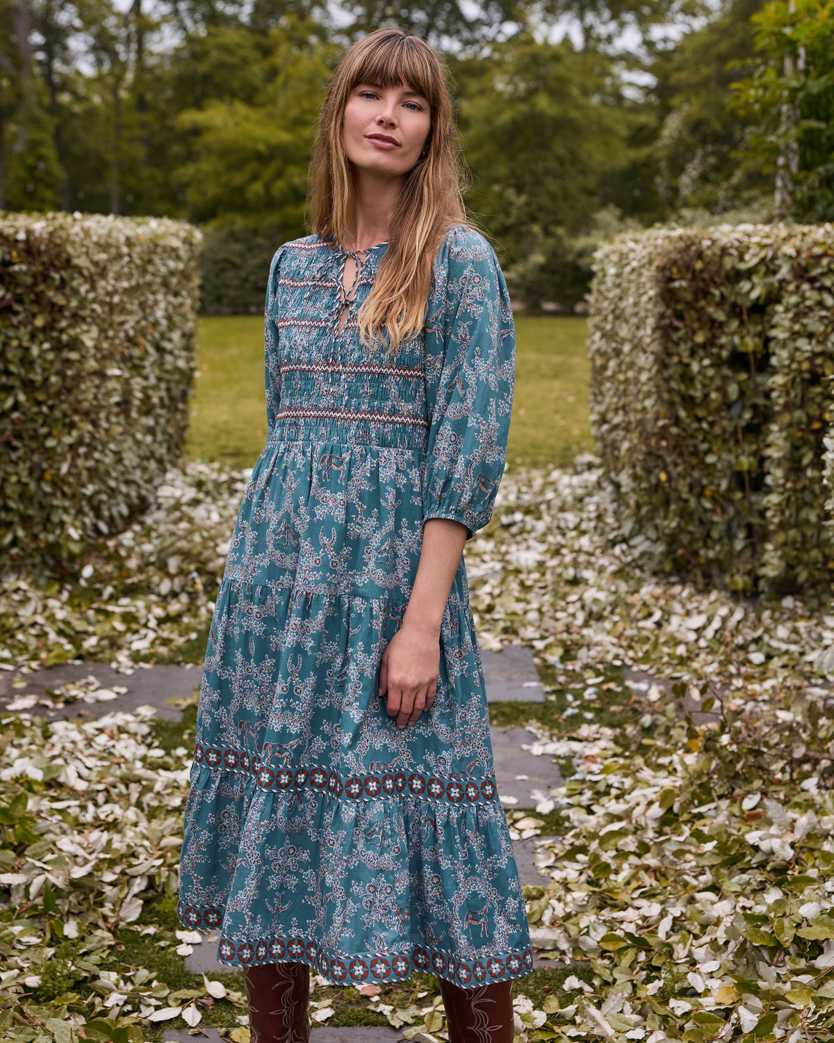 Front view of the Riverstone Hudson Dress showing its patterned print, smocked bodice, bow detail, full sleeves, and midi length.