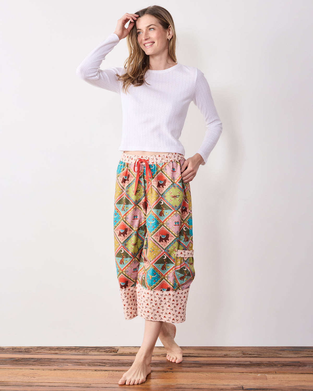 Full view of a model wearing the patterned cropped pants with a white long-sleeve top, drawstring waist, and side pocket.