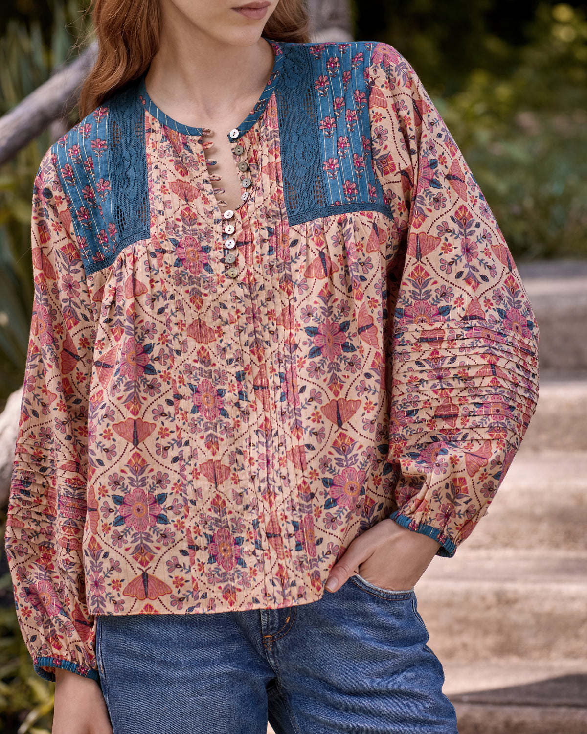 Close-up of the Winged Tapestry Denver blouse showing its floral print, blue yoke panels, decorative buttons, and gathered sleeves.