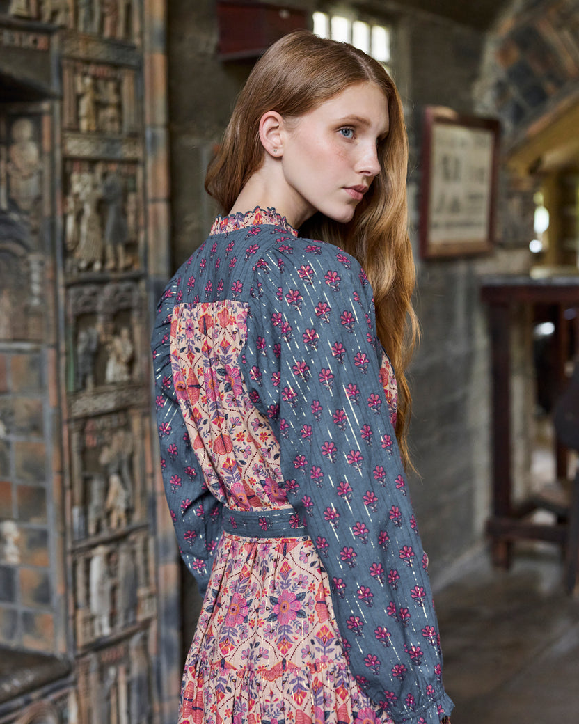 Back three-quarter view of the Winged Tapestry Lauren dress, showing the dark floral sleeves, patterned back panel, waist tie, and tiered skirt.