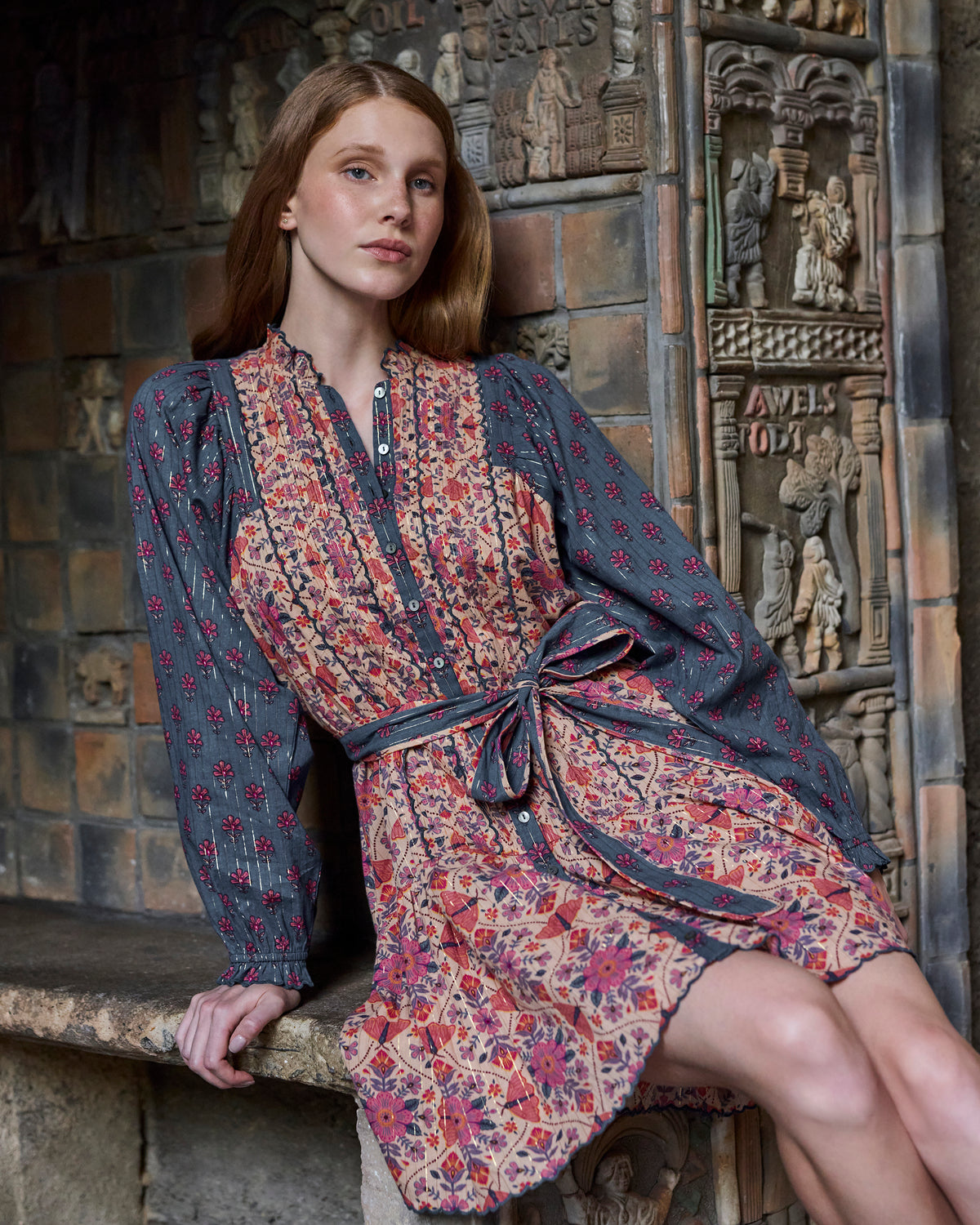 Seated front view of the Winged Tapestry Lauren dress, highlighting the button placket, tied waist, floral print, and scalloped skirt hem.