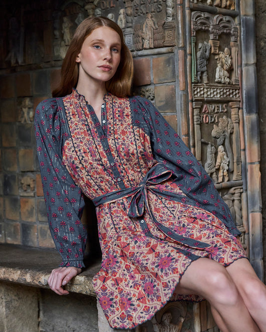 Seated front view of the Winged Tapestry Lauren dress, highlighting the button placket, tied waist, floral print, and scalloped skirt hem.