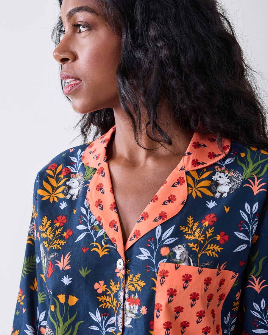 Close-up of the indigo Woodland Critters pajama top showing the coral notched collar, patterned chest pocket, button, and woodland print.