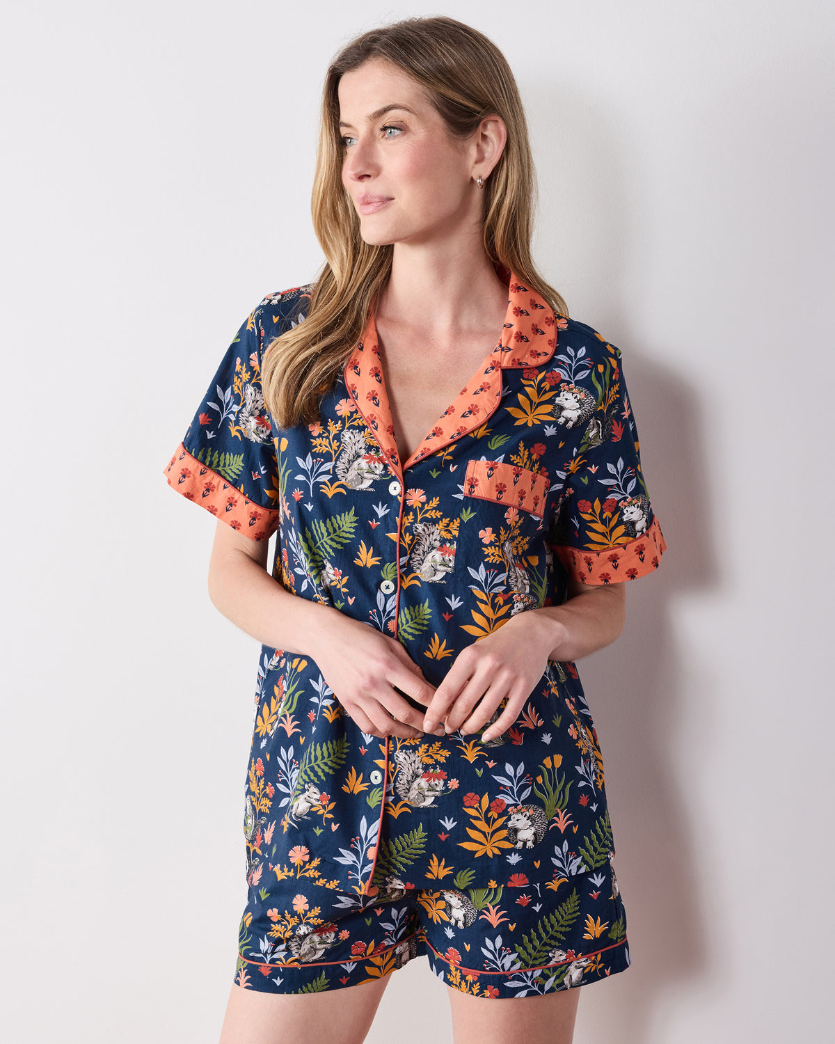 Front view of the indigo Woodland Critters short pajama set with a button-front top, coral contrast trim, chest pocket, and matching shorts.