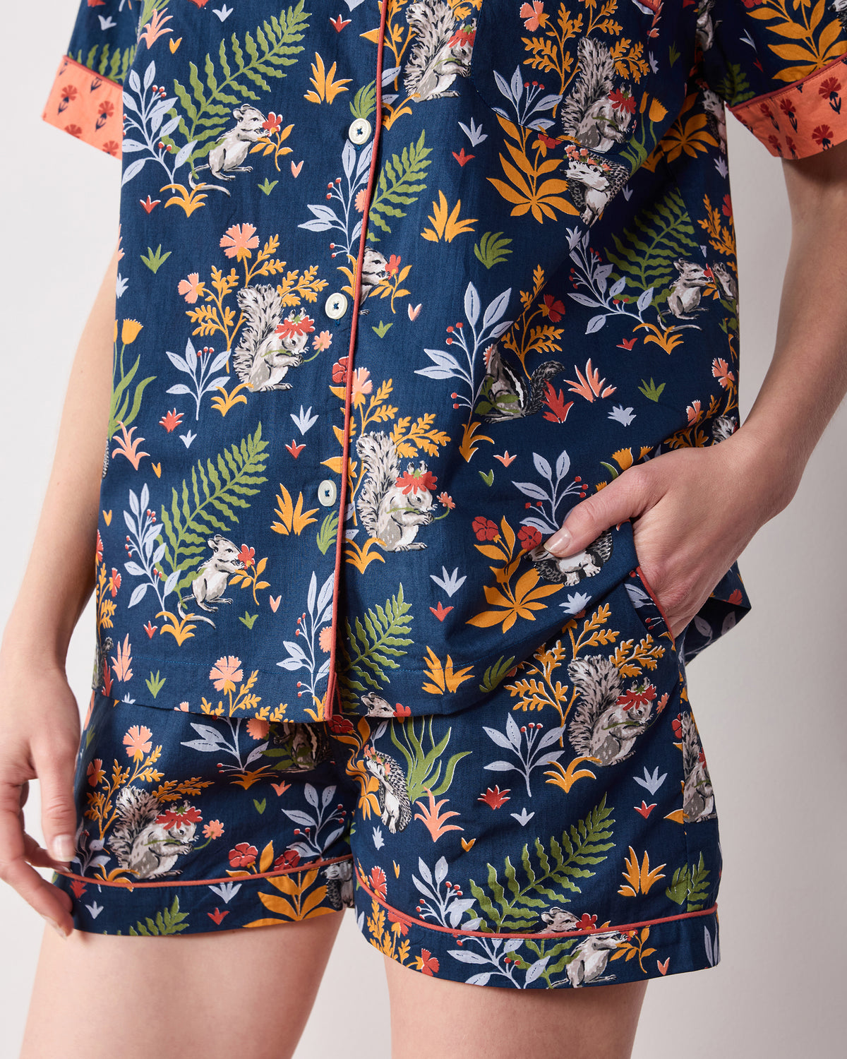 Close-up of the indigo Woodland Critters short pajama set, showing the button-front top, coral sleeve cuffs and piping, chest pocket, and shorts pocket.